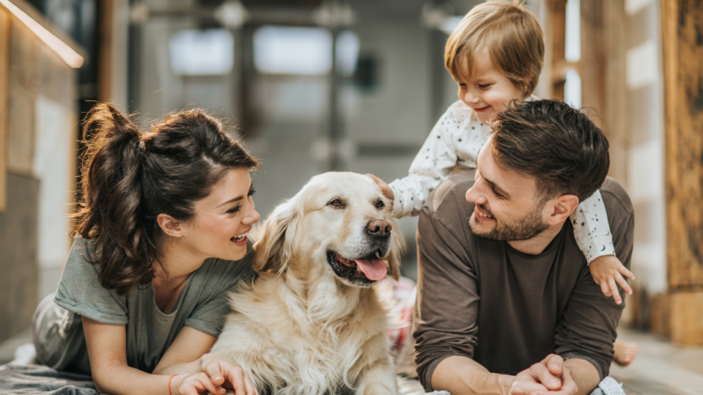 A happy family with a golden retriever, all smiling and lying on the floor together.